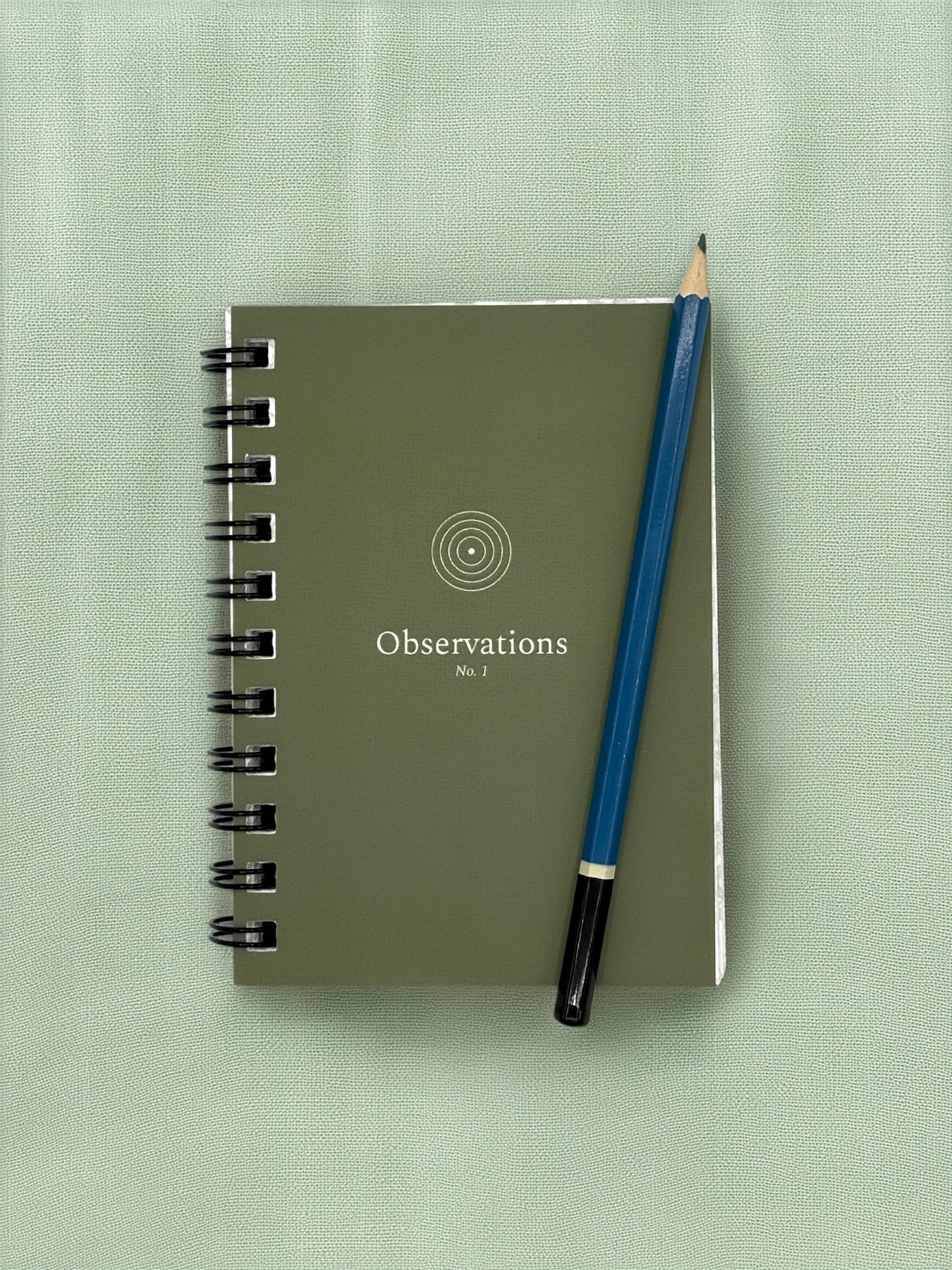 Sage green cover of Observations No. 1 with a small concentric-circle emblem and a drawing pencil